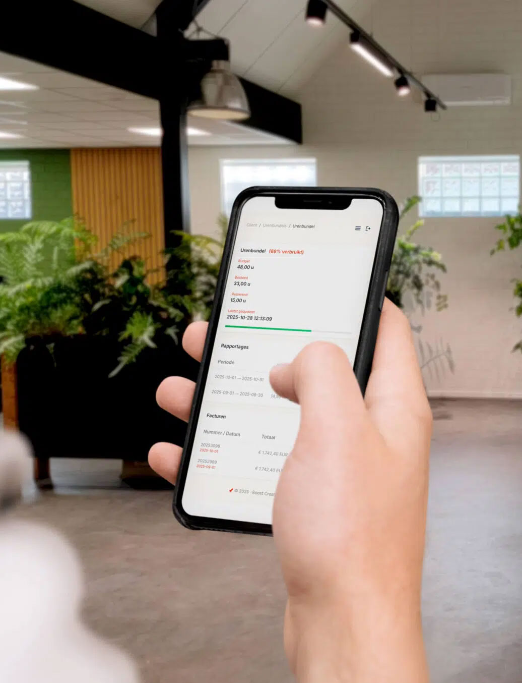 Een telefoon in een hand met het Boost Creators kantoor op de achtergrond.