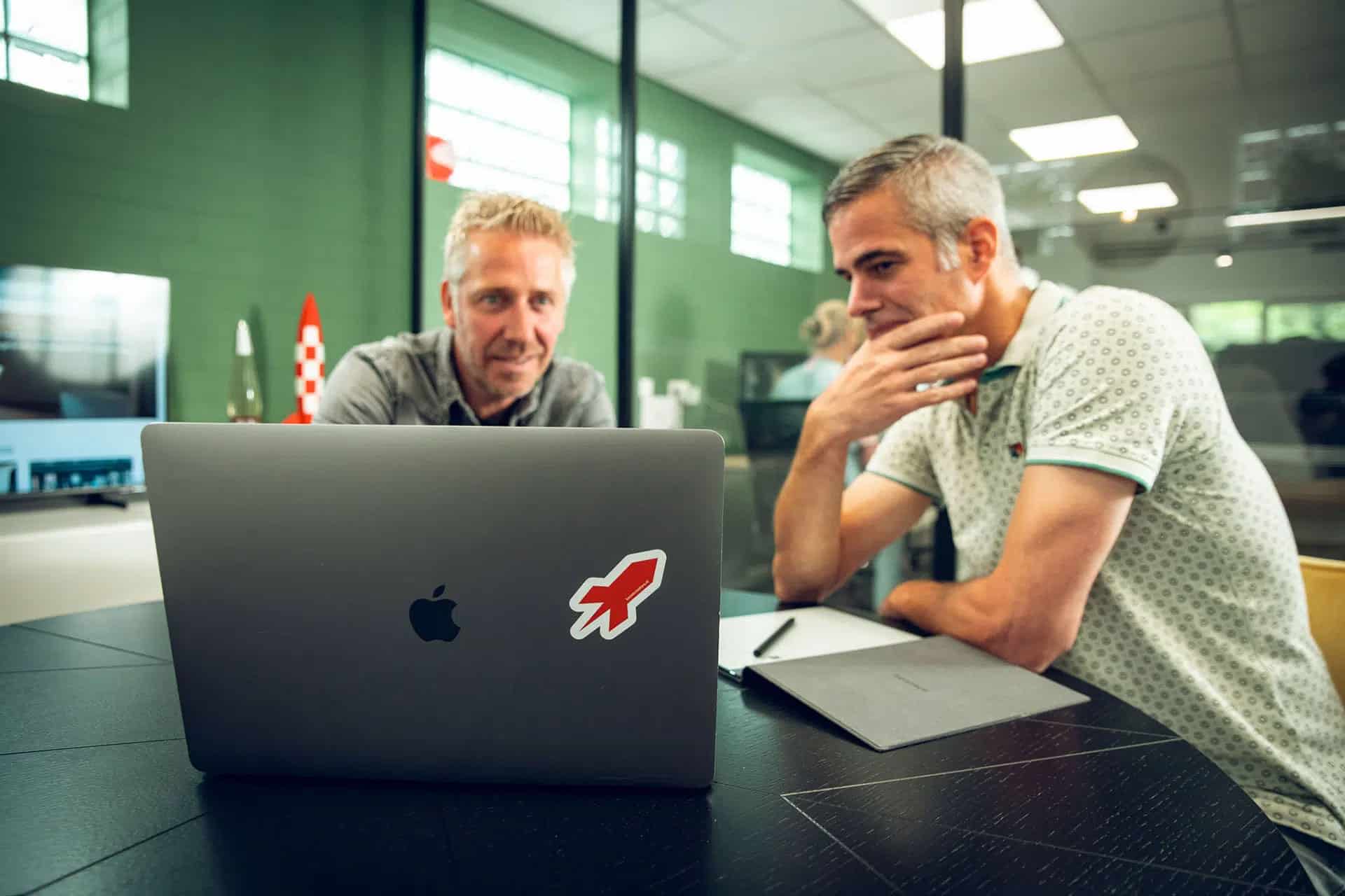 2 Collega's in overleg achter een laptop met het Boost Creators logo op de laptop.