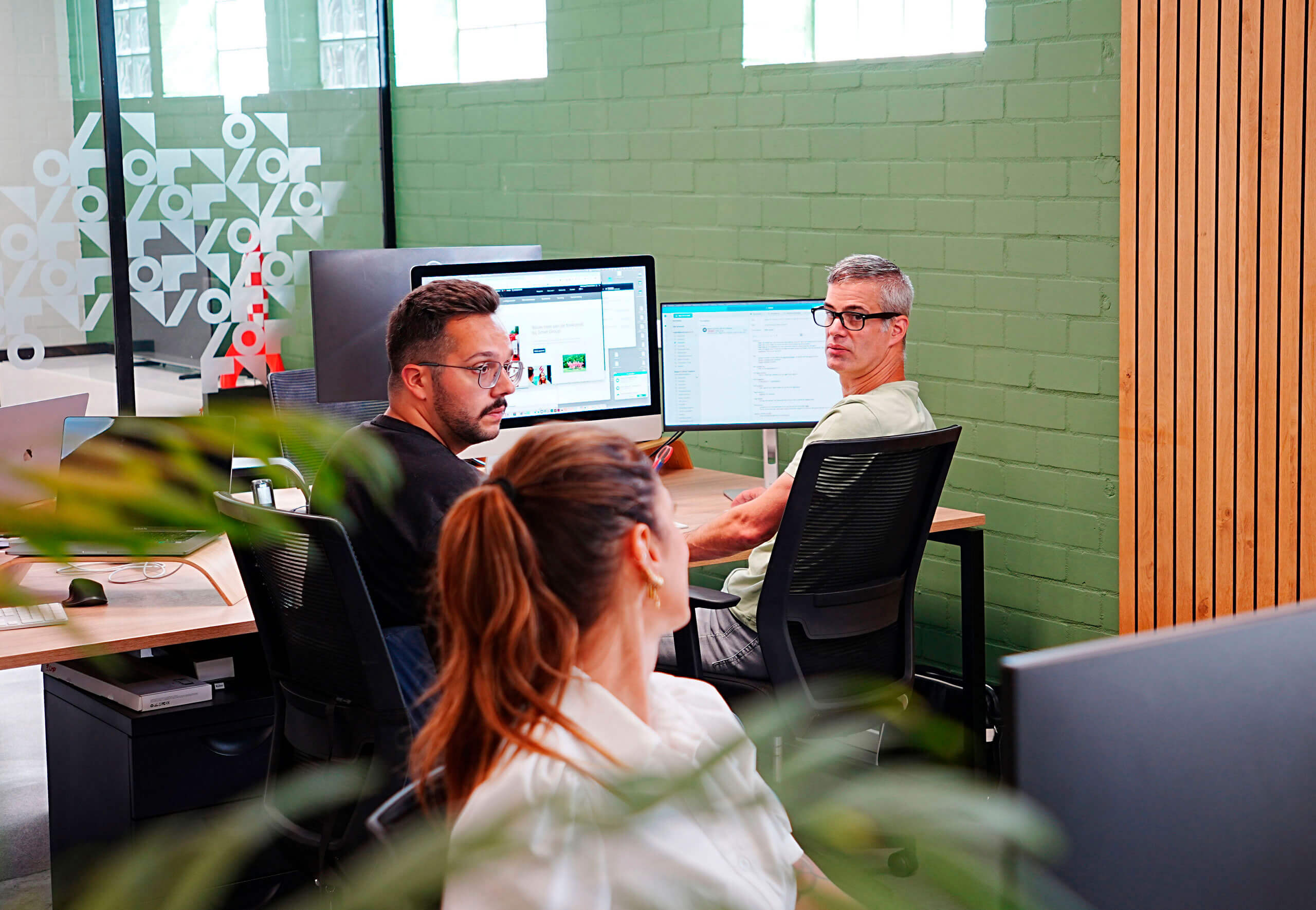 3 collega's die overleggen achter hun computer schermen.