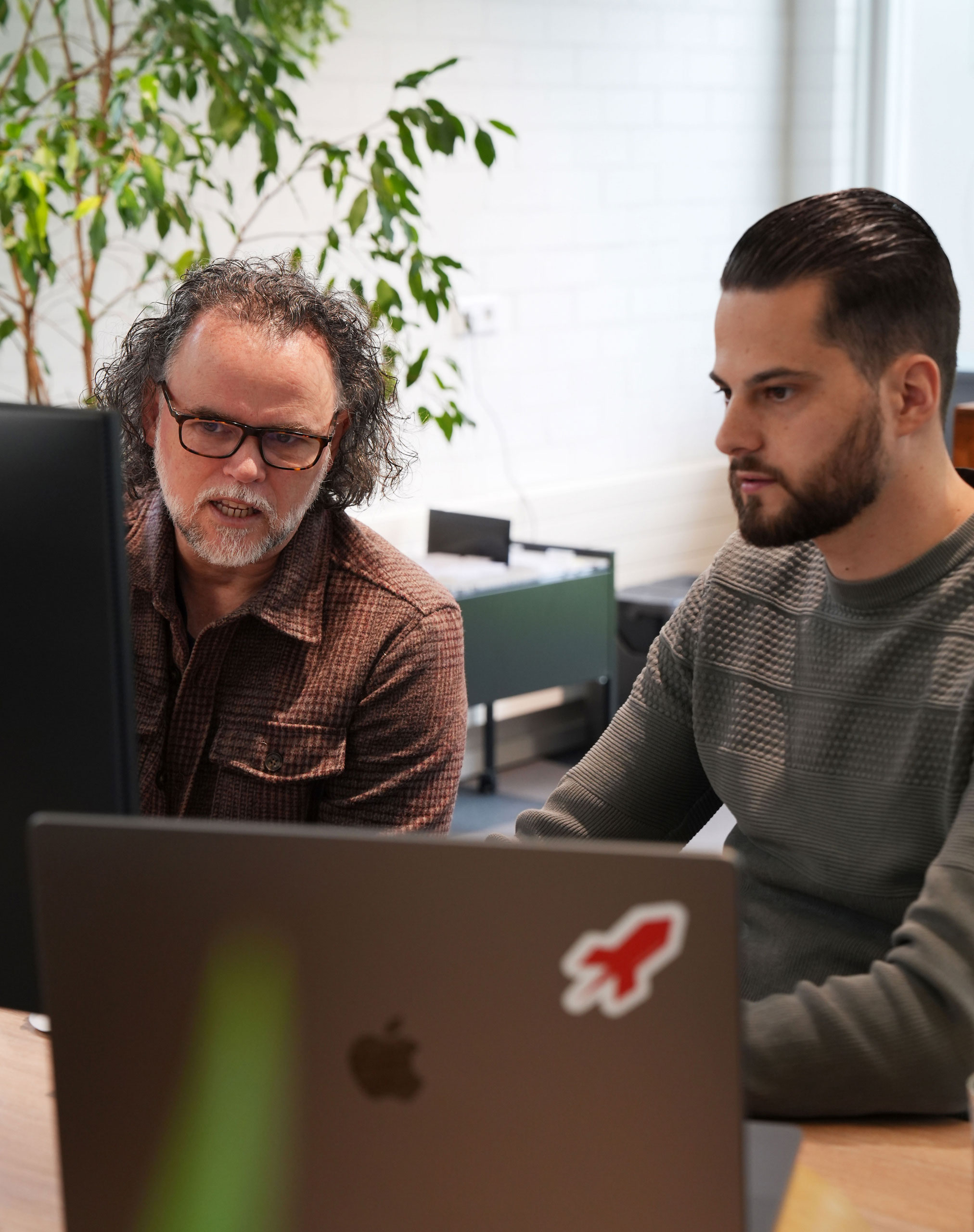 Tom en Stefan overleggen over branding achter de computer.